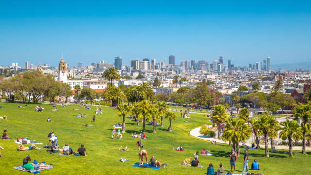 People enjoying the sunny weather in Mission Dolores park on a beautiful day with clear blue skies with the skyline of San Francisco in the background