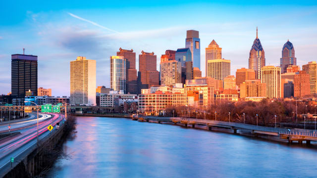 Late afternoon in Philadelphia. The skyline glows under an orange sunset light. Schuylkill expressway traffic runs parallel to Schuylkill river.