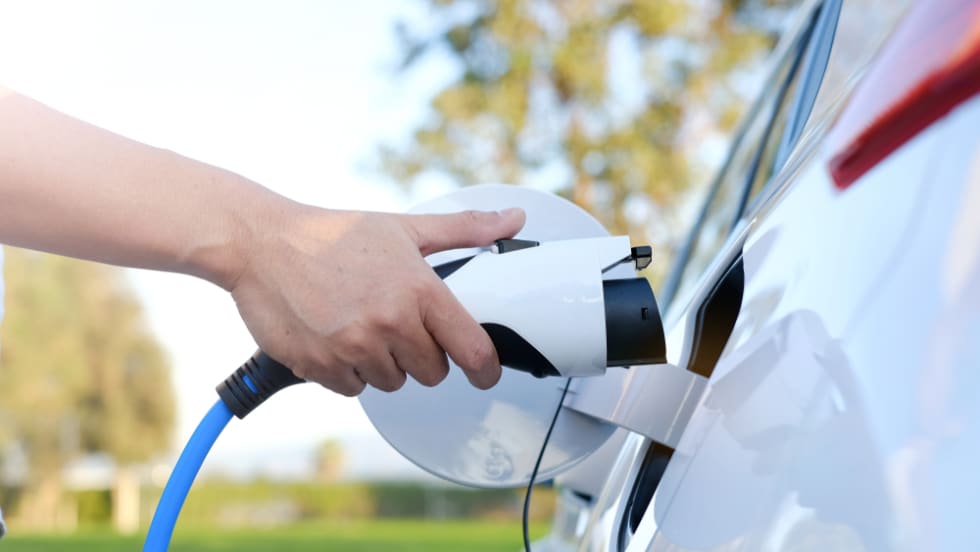 Electric car or ev is charging at station . man use the white power cable and plug on nature background. eco and clean energy concept with the mobile phone smart technology. zero gas no transmission