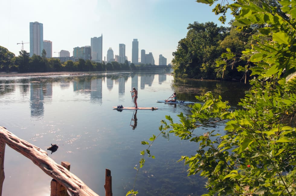 Two females paddle boarding on Ladybird Lake with downtown Austin, TX in the background.