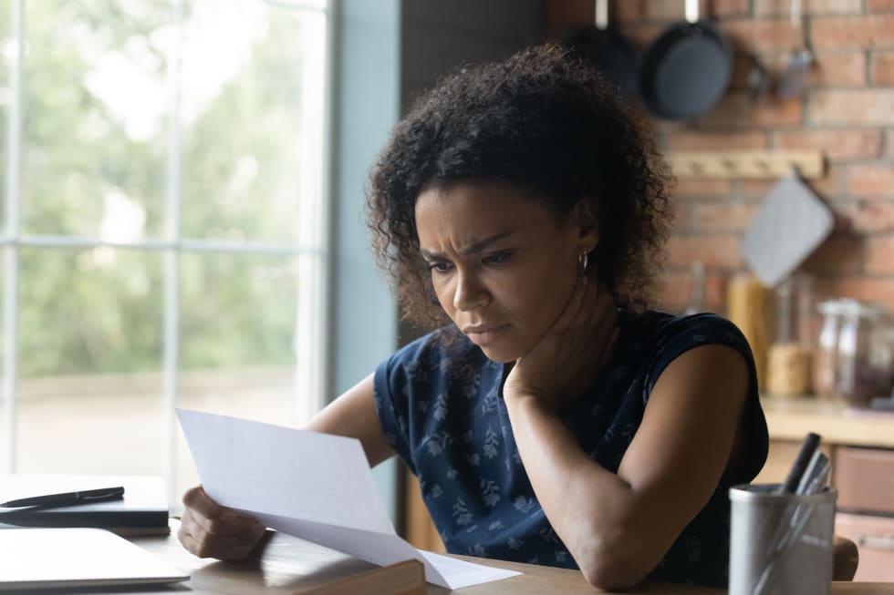 woman reading paper letter with bad news, stressed of getting bank debt or loan rejection notification, feeling confused of termination notice, sitting at table.