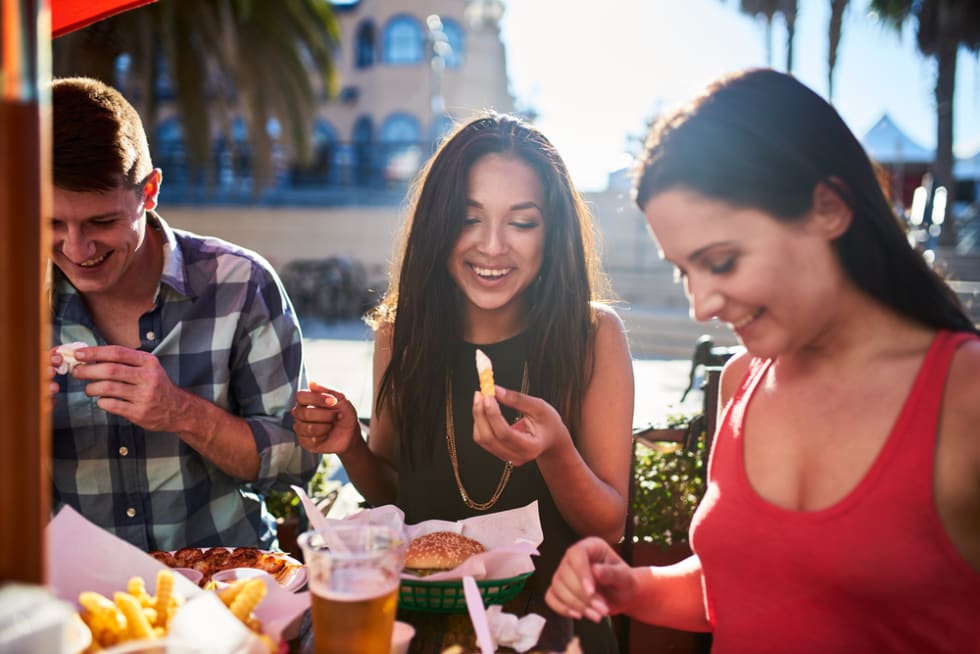 friends eating french fries and hamburgers together at outdoor restaurant under summer sun