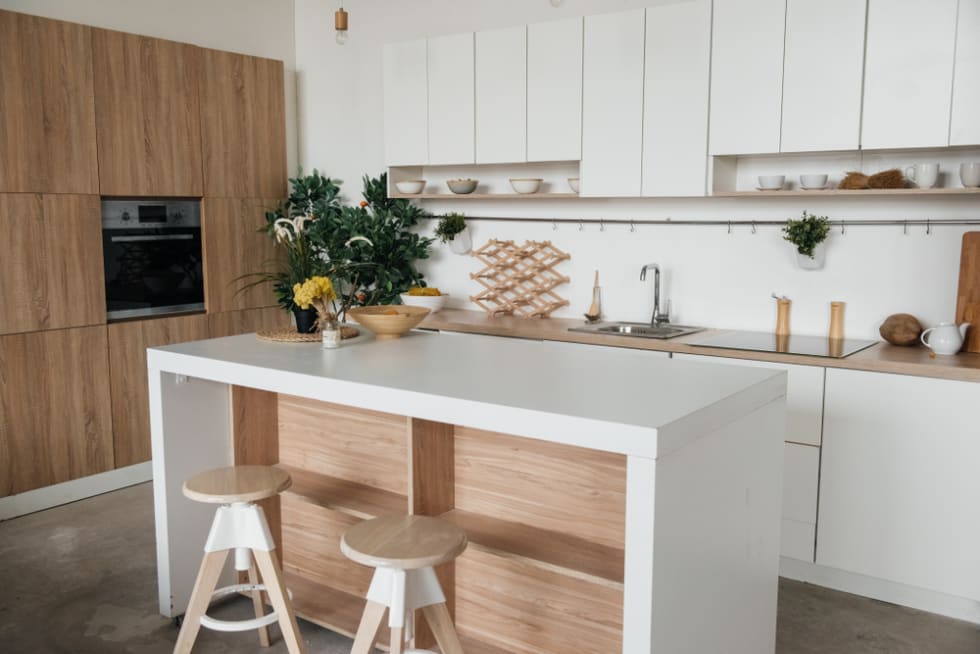 Stylish kitchen in white and brown wood. Style minimalism. Sink, table top, plants, pot, shelf for dishes. Bar stools, table.