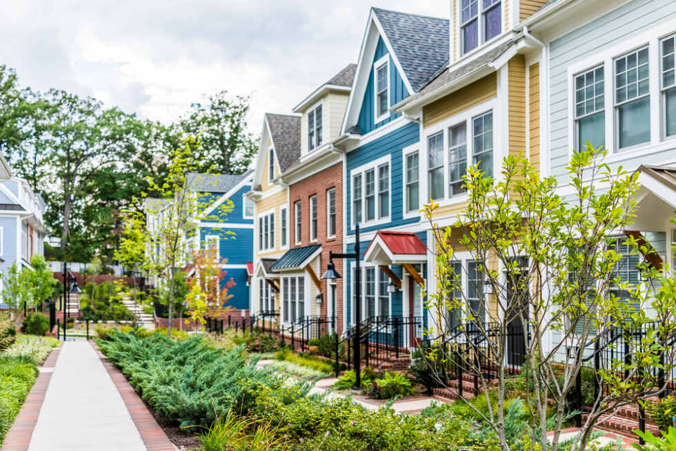  Row of colorful, red, yellow, blue, white, green painted residential townhouses, homes, houses with brick patio gardens in summer