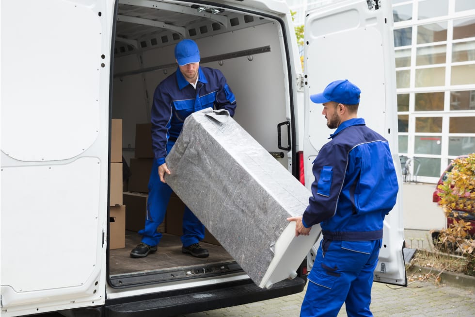 Two Young Delivery Men In Uniform Unloading Furniture From Vehicle - free furniture pick-up