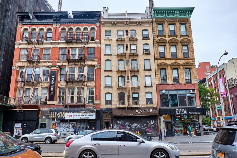 Cars driving by the facades of some buildings on Bowery Street in Lower Manhattan