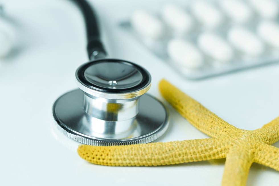 closeup of a yellow starfish on a doctors office, next to a computer keyboard, a stethoscope and some pills