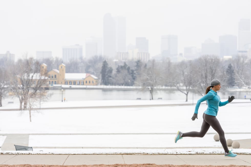 Young woman running jogging in snow blanketed City Park with Denver Colorado skyline in background