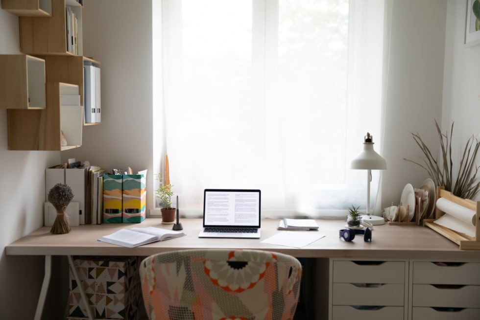 Empty desk workplace in cozy home bedroom with open laptop, books and paperwork
