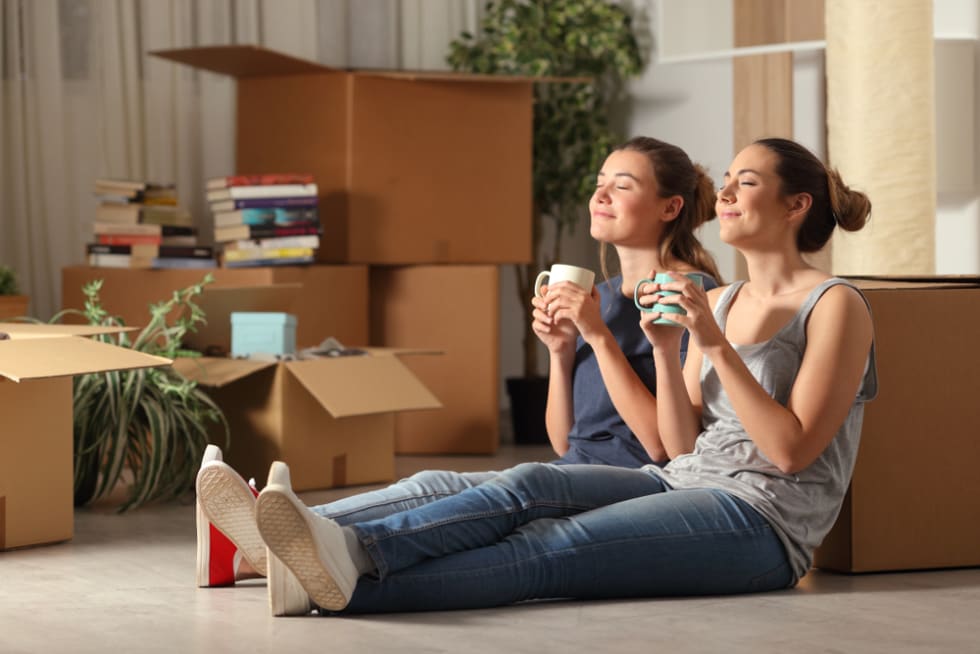 Two happy roommates moving home resting breathing fresh air sitting on the floor in the night