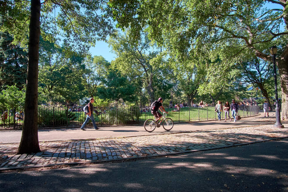 People walking and cycling in Tompkins Square Park in East Village on a warm October day