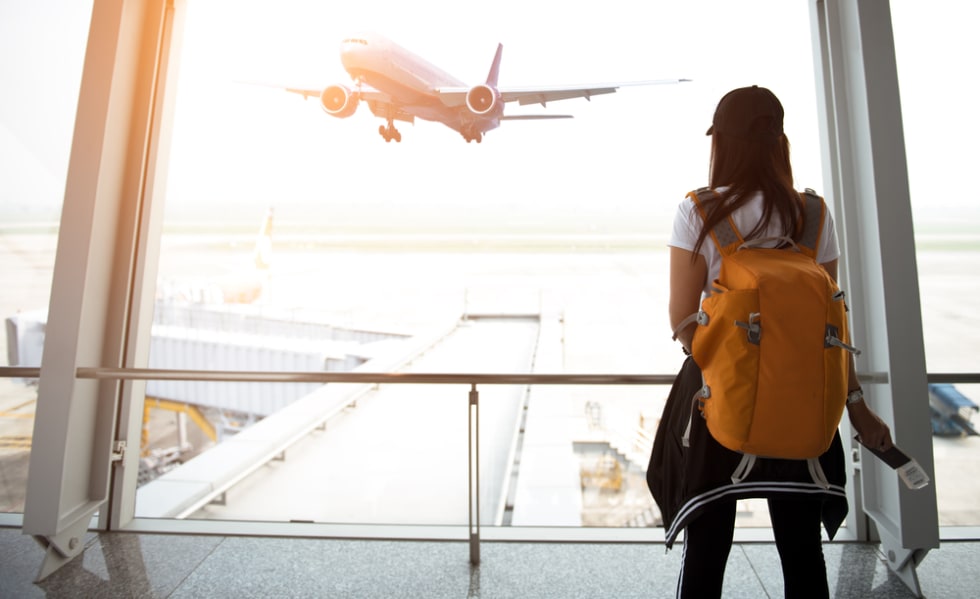 Traveler woman plan and backpack see airplane flight at the airport glass window