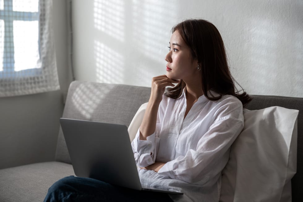 woman thinking for the future and confuses of online working on a laptop computer at home sitting on a sofa - avoid rent increase