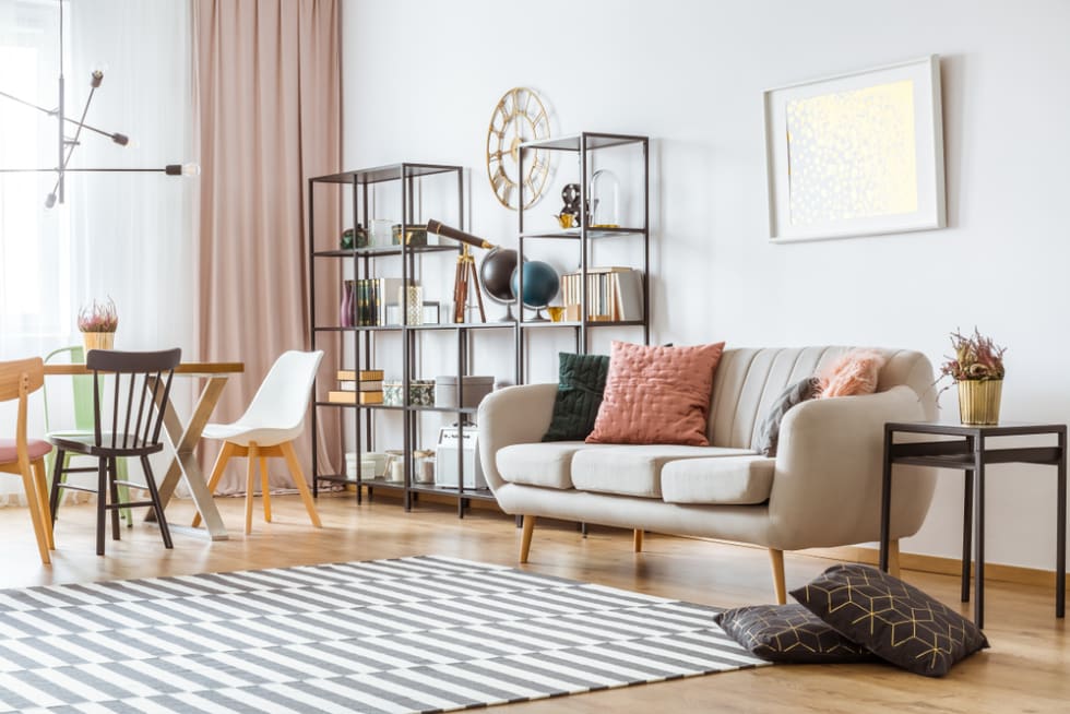 Painting on white wall above sofa with cushions in living room interior with chairs at the table under metal lamp