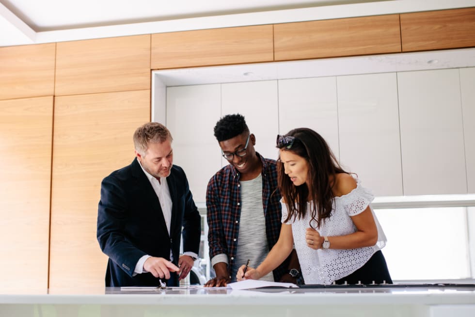  Couple signing a contract documents while standing inside a house with real estate agent.