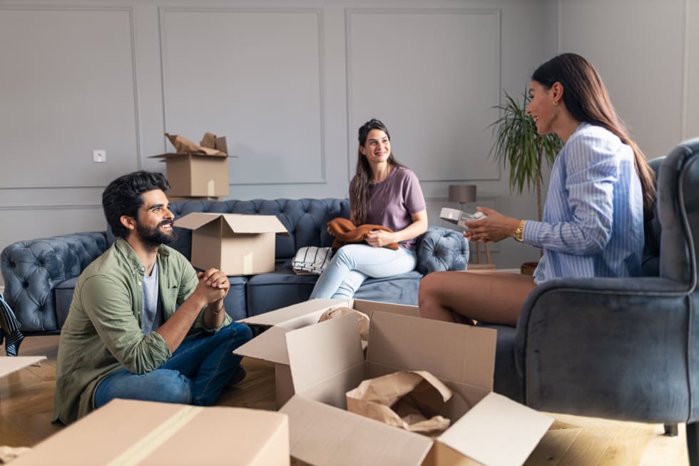 Friends sitting and talking in their new apartment while unpacking their things from cardboard box - roommate agreement