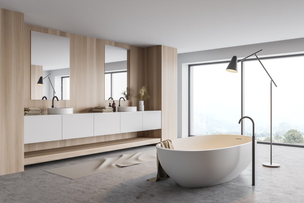 Corner of panoramic bathroom with white and wooden walls, concrete floor, comfortable white bathtub and double sink standing on white countertop. Window with blurry mountain view.
