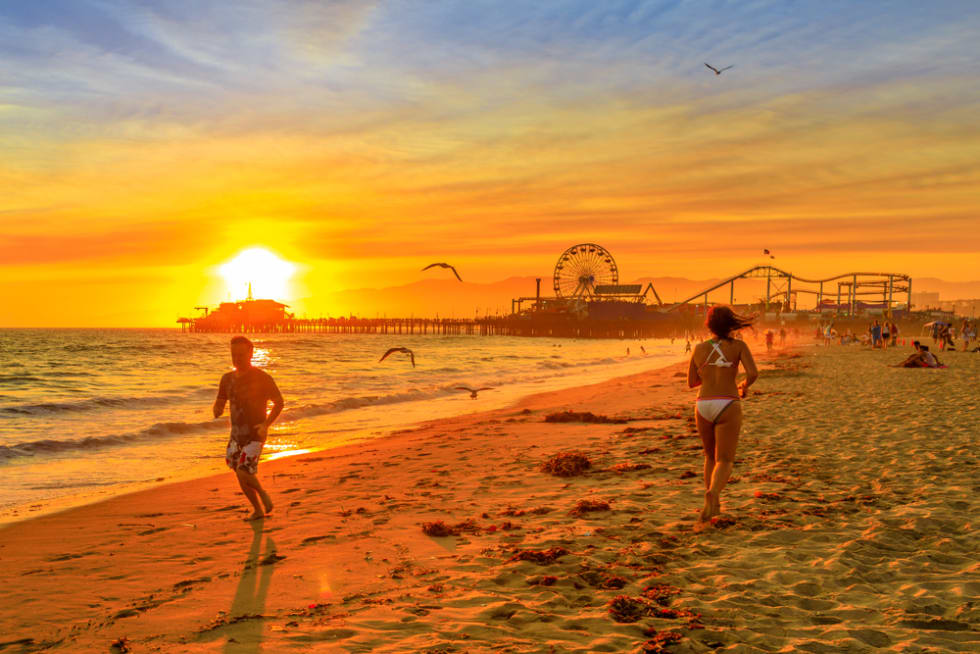 People running on seashore of Santa Monica Pier, Pacific Coast. Amusement park, ferris wheel 