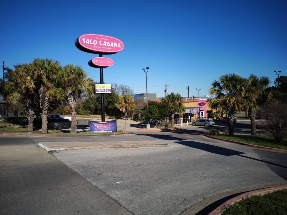the entrance to a Taco Cabana with festive palm trees on either side