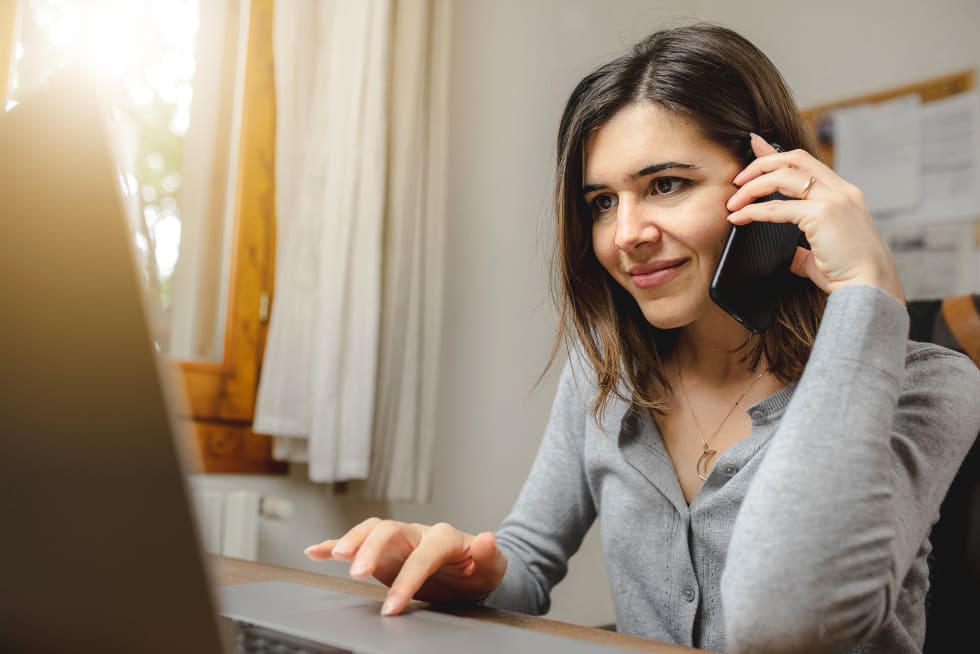 woman talking on the phone while working on computer in desk office. Searching on internet - free furniture pick-up