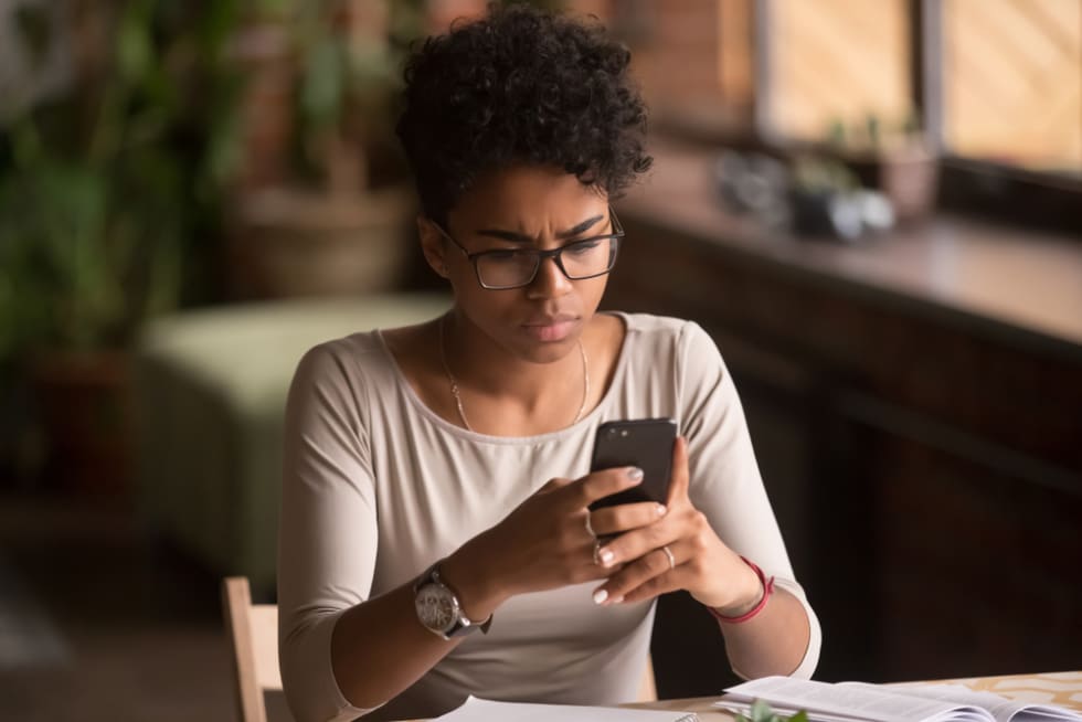 Upset confused african woman holding cellphone having problem with mobile phone,