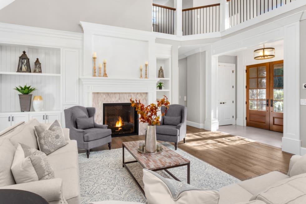 Beautiful living room in new traditional style luxury home. Features vaulted ceilings, fireplace with roaring fire, and elegant furnishings. Shows foyer front door.