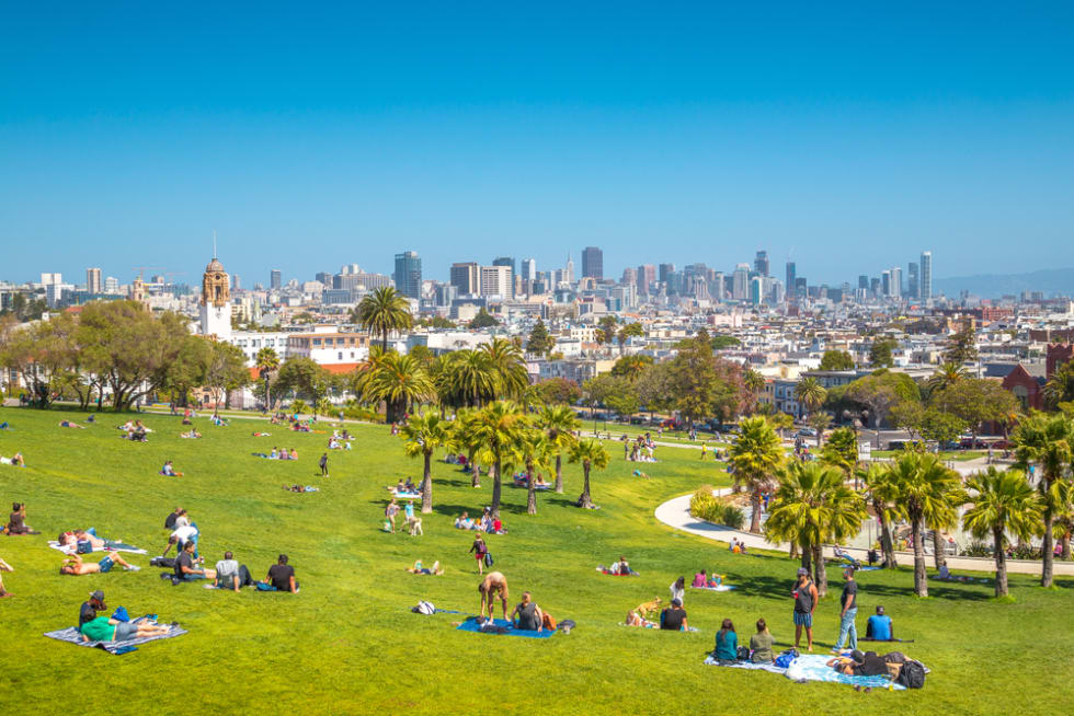 People enjoying the sunny weather in Mission Dolores park on a beautiful day with clear blue skies with the skyline of San Francisco in the background