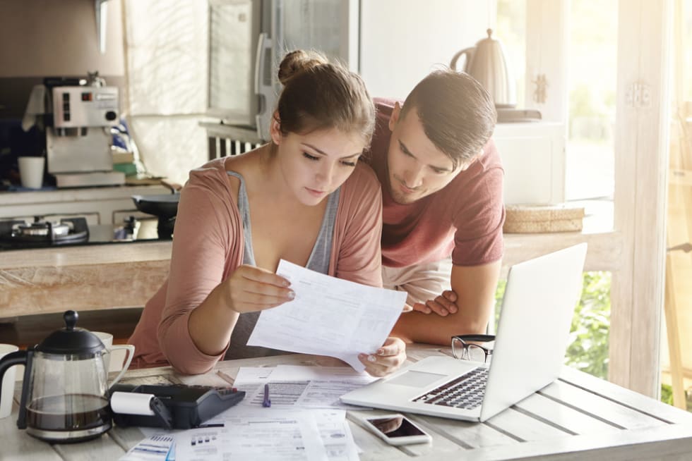 Young couple managing finances, reviewing their bank accounts using laptop computer and calculator at modern kitchen