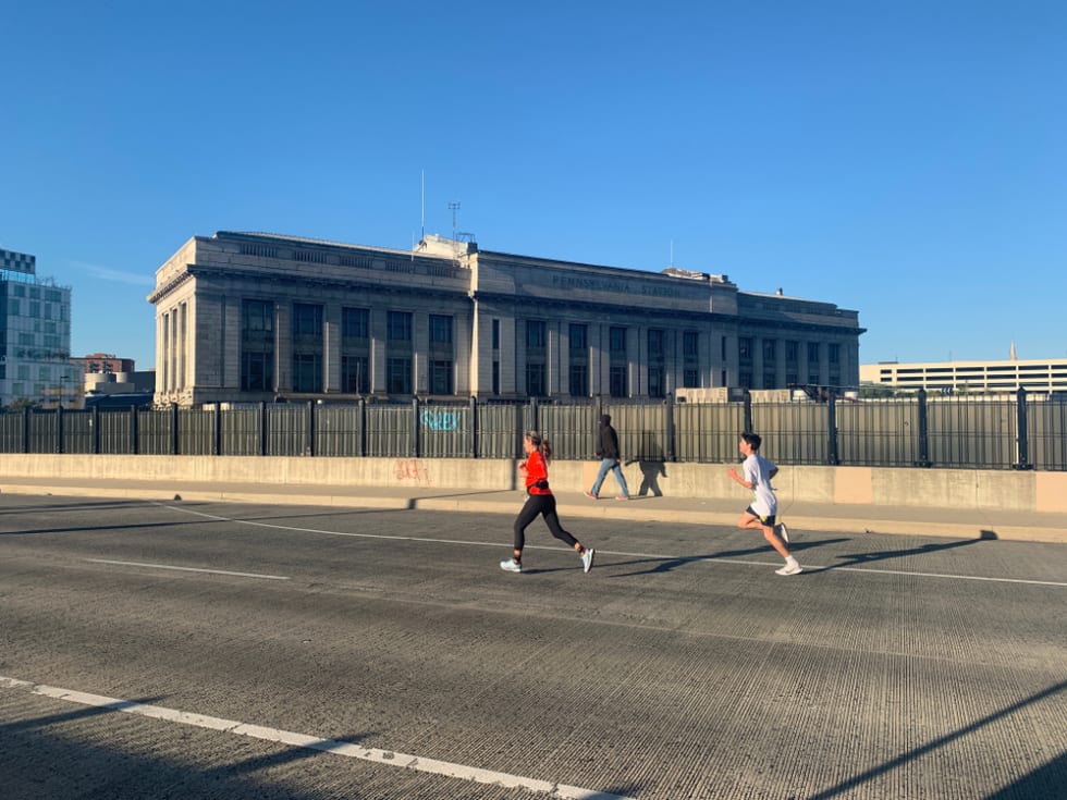 Two runners and a pedestrian travel southbound on St Paul st with Pennsylvania station in the background during the Baltimore running festival