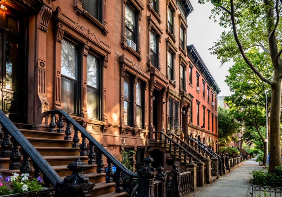 Scenic view of a classic Brooklyn brownstone block with a long facade and ornate stoop balustrades on a summer day in Clinton Hills, Brooklyn