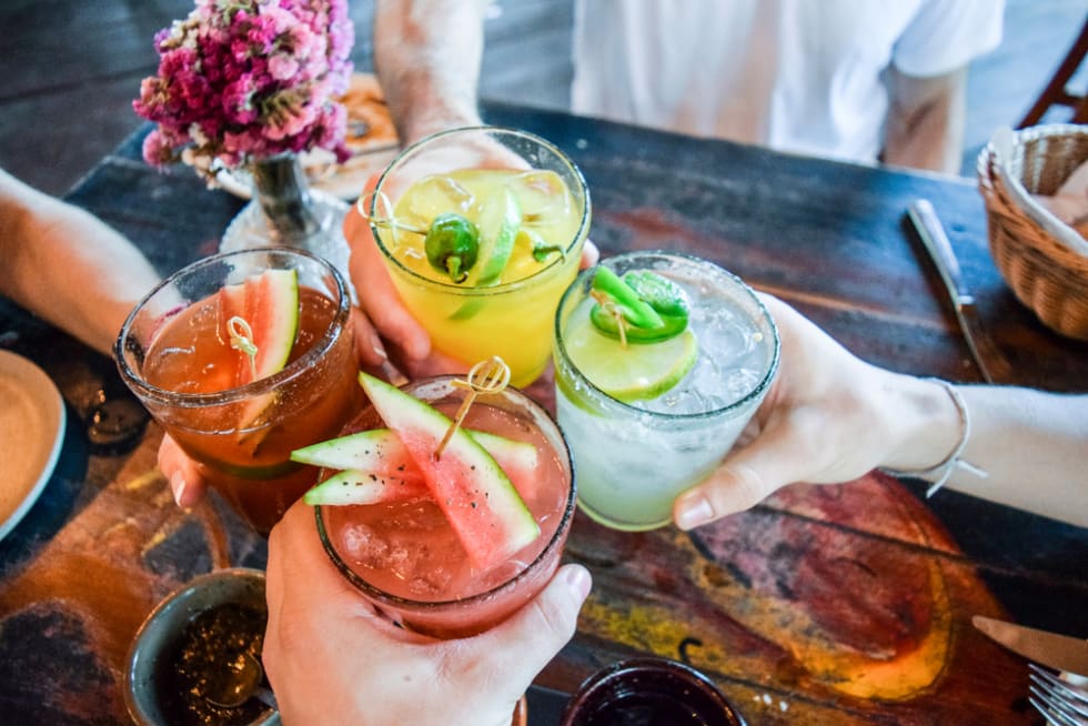 Friends toasting, saying cheers holding tropical blended fruit margaritas. 