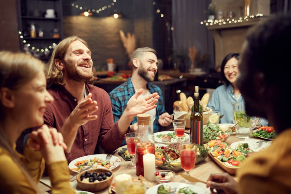 young people enjoying dinner party with friends and smiling happily sitting at table in dimly lit room, copy space