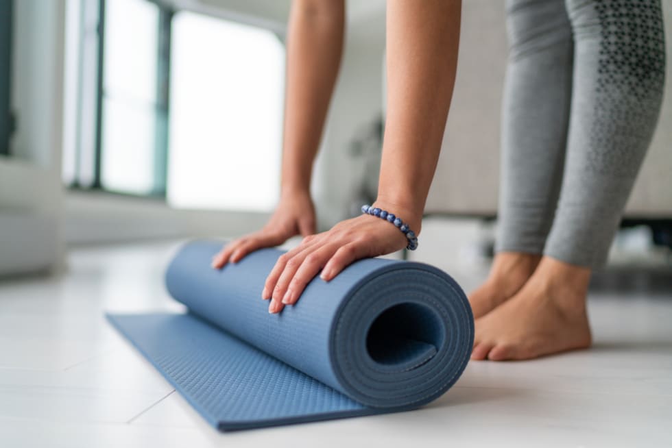 Yoga at home woman rolling exercise mat in living room of house or apartment condo for morning wellness yoga practice.