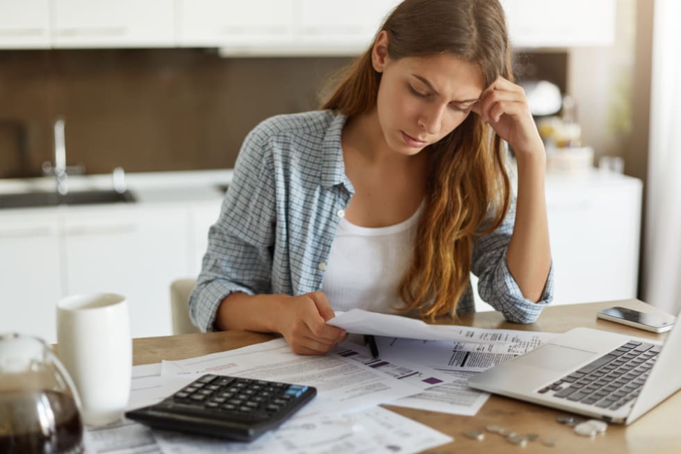 Indoor shot of casually dressed young woman holding papers in her hands, calculating family budget,