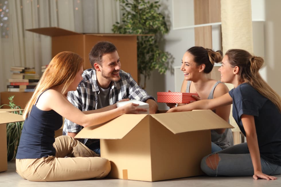 Happy roommates unboxing belongings moving home sitting on the floor in the night