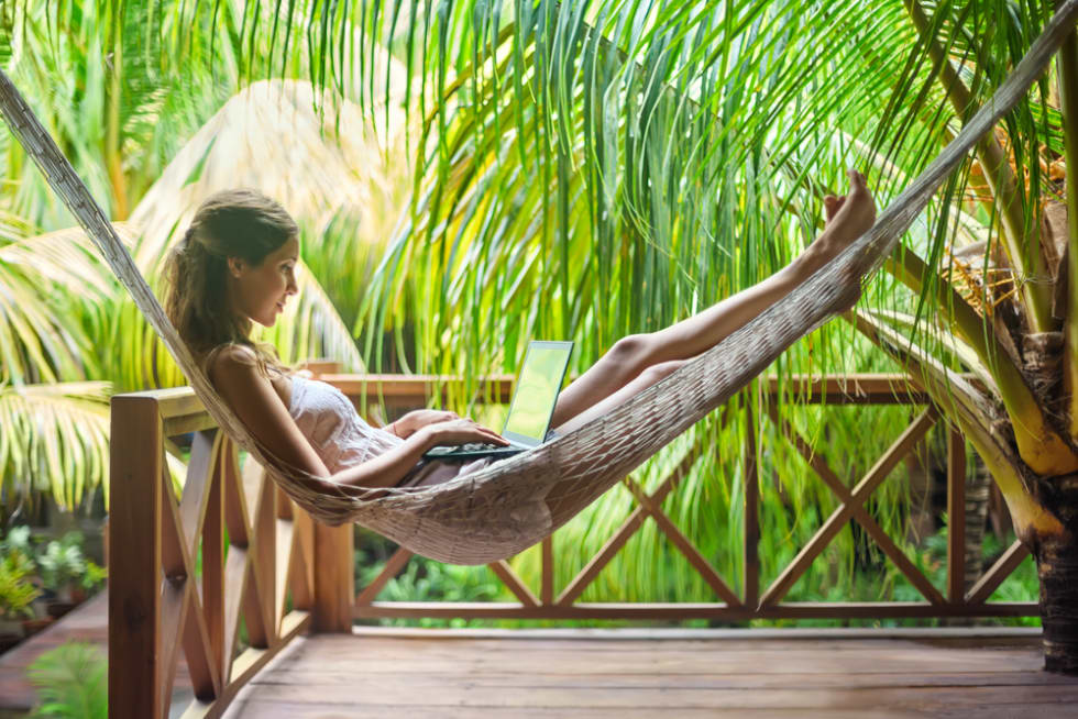 woman lying in a hammock with laptop in a tropical resort