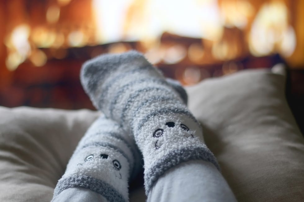 Feet in cute fuzzy socks in front of a fireplace.