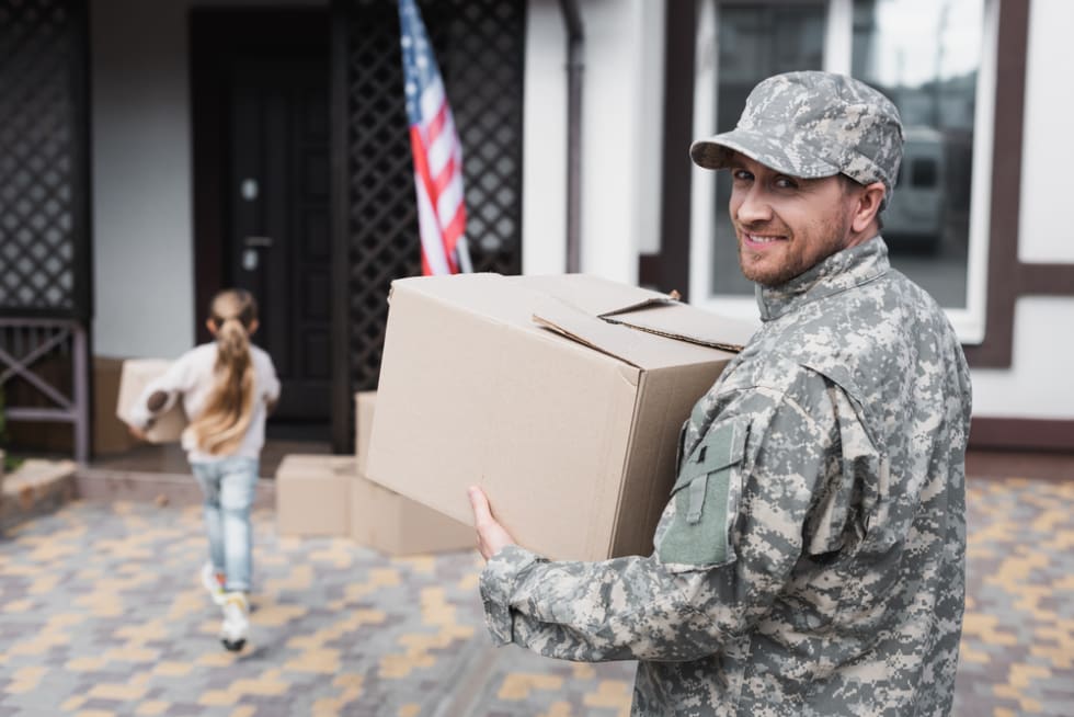  Happy military serviceman holding cardboard box and looking at camera with blurred girl on background