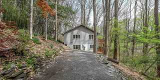 Welcome home! One of a kind, strikingly designed 2-level hillside chalet built on 1 1/2 acres of wooded property with stream surrounded by park land. Gallery 1